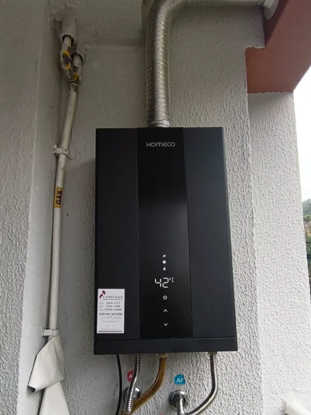 Aquecedor a gás Komeco preto instalado pela Configás em varanda, com chaminé e tubulação de gás identificada