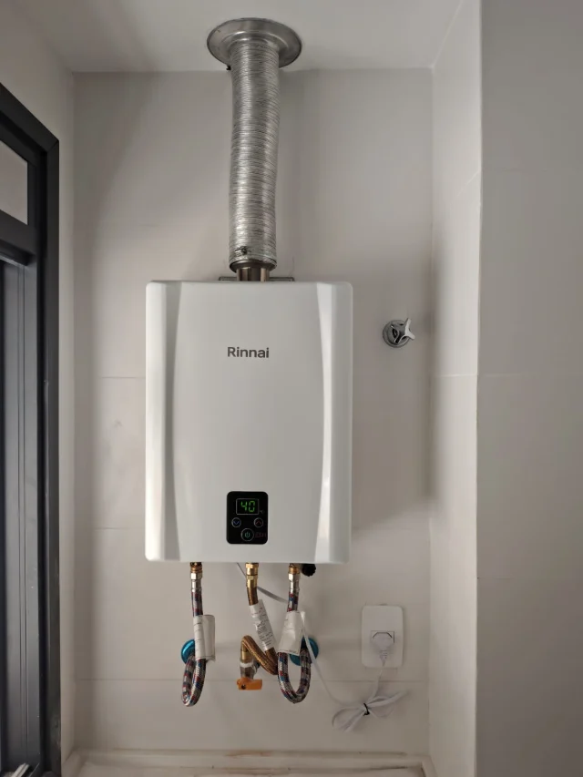 Aquecedor a gás Rinnai digital branco instalado pela Configás, com chaminé até o teto e ligações flexíveis de água e gás