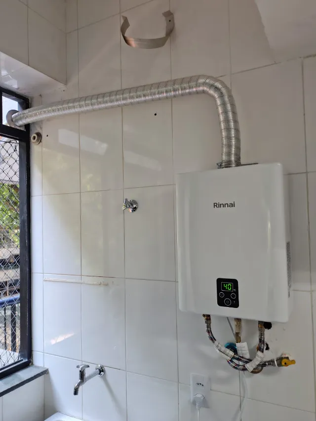Aquecedor a gás Rinnai digital instalado em área de serviço, com chaminé horizontal até a janela