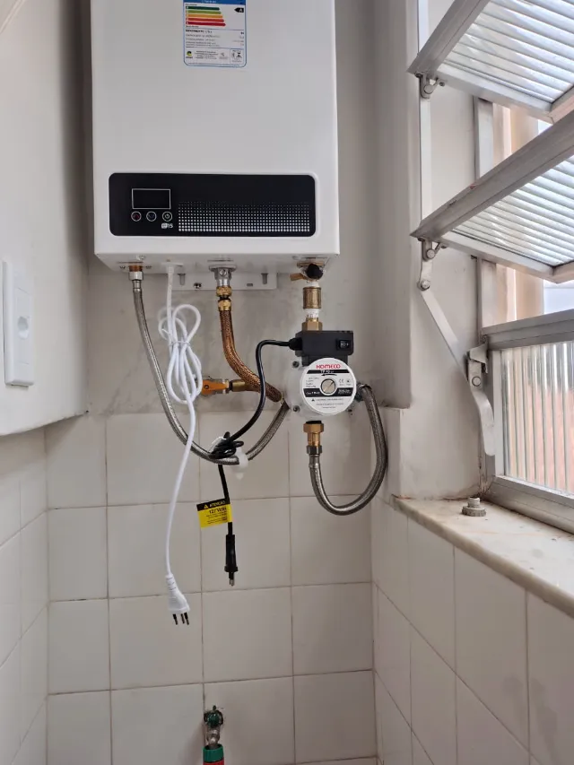 Pressurizador Komeco TP 40 instalado na saída de água quente de um aquecedor a gás Rinnai E15, com ligações flexíveis