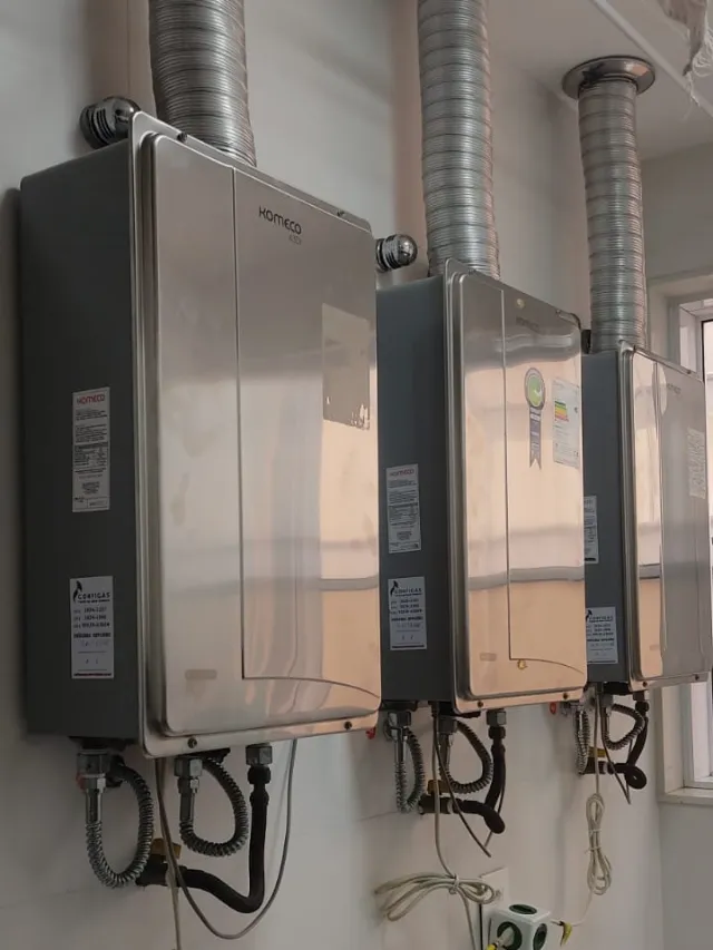 Três aquecedores a gás Komeco em área técnica, com etiquetas de revisão da Configás