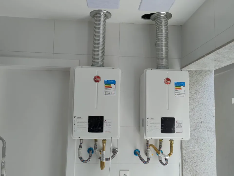 Dois aquecedores a gás Rheem digitais de 45 litros instalados lado a lado, com chaminés no teto e etiquetas de revisão da Configás